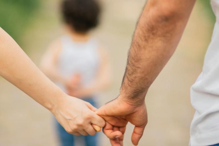 Parents holding hands in the foreground while their child walks ahead of them.