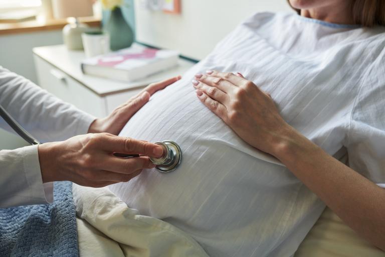 A pregnant woman in a bed while a doctor places a stethoscope on her belly.