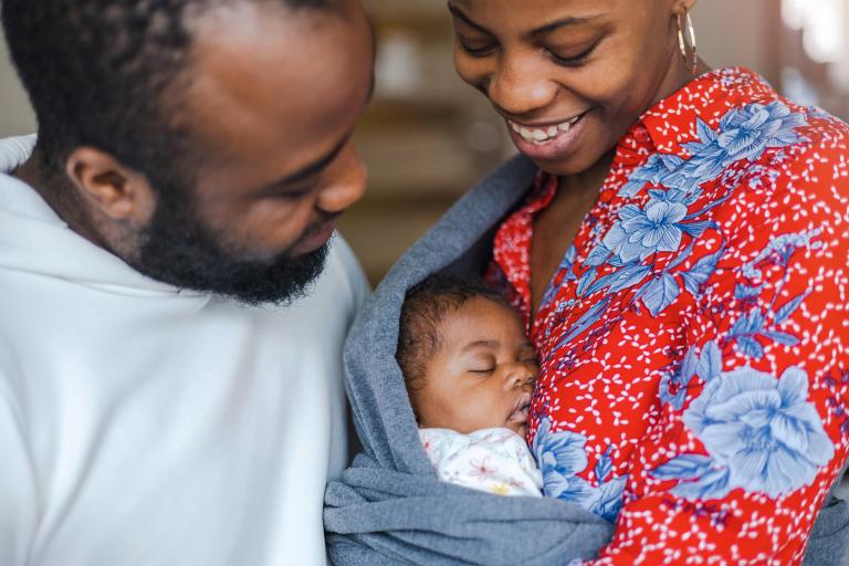 A newborn baby in a sling between their parents.