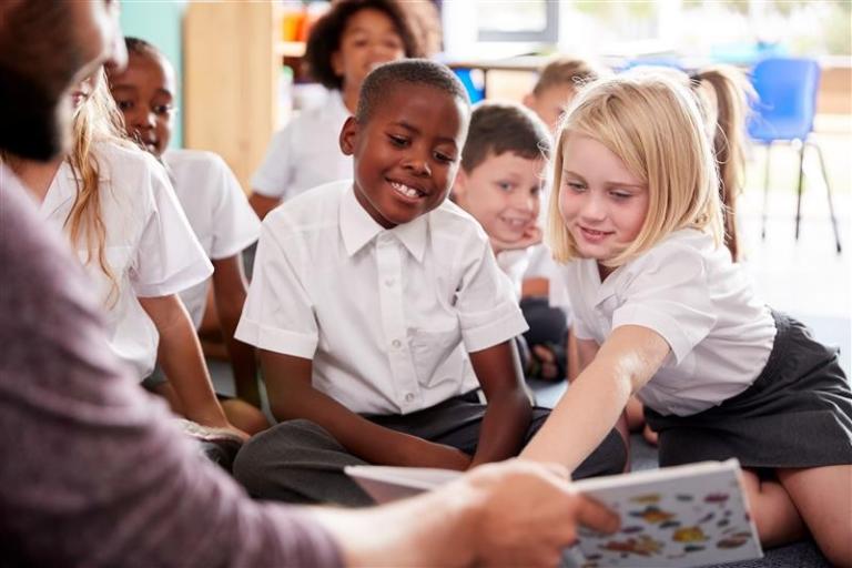 Children smiling and reading a book with a teacher, they are wearing school uniform