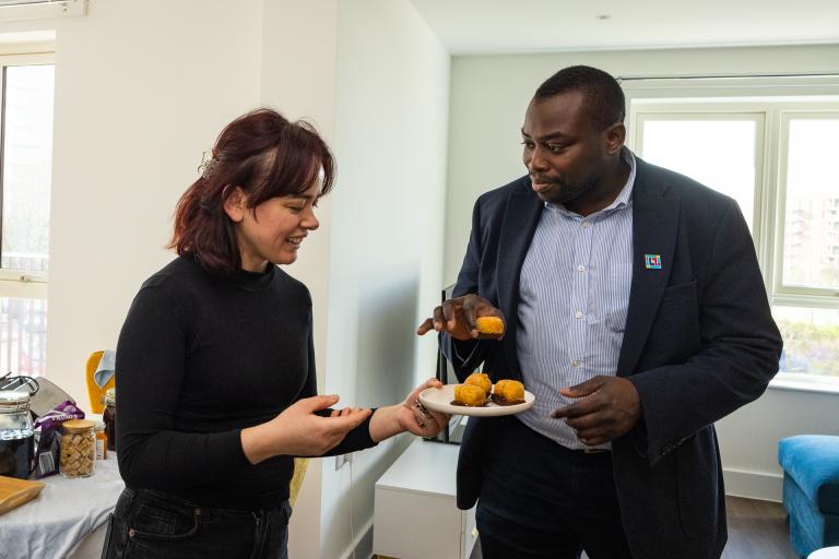 A new council tenant at Kidbrooke Park Road South offers a home made cake to leader of the council Councillor Anthony Okereke