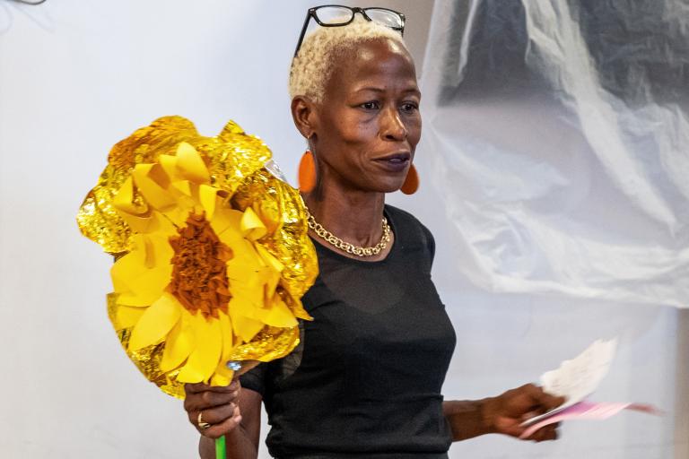 A woman holding a large yellow flower that has been made out of paper.