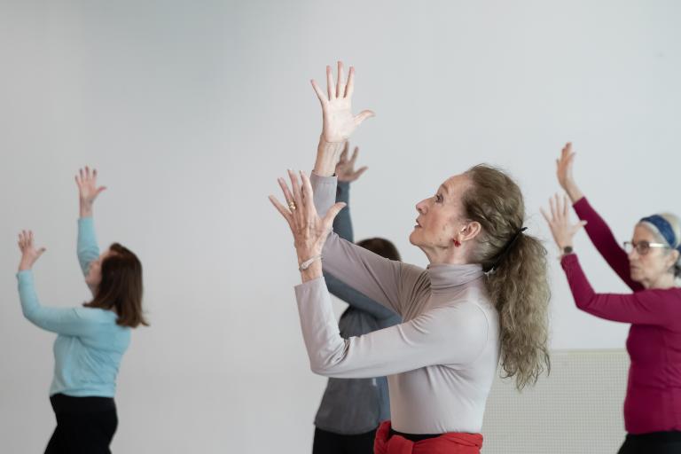 A group of women standing in a dance formation with their hands up to one side.