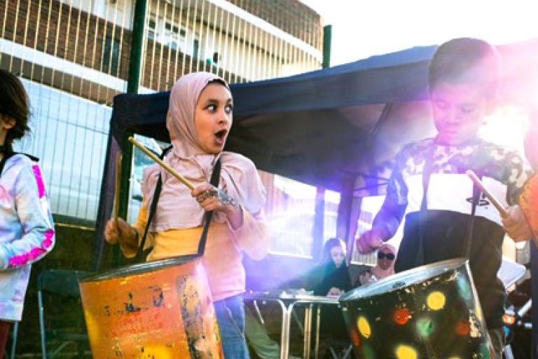 A troop of young children drumming on large colourful drums. 