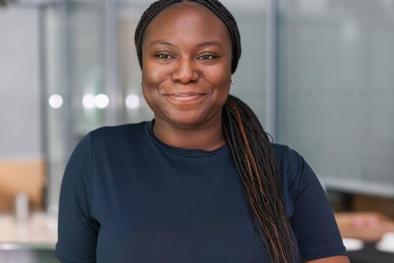 A woman in a navy dress smiles looking to camera 