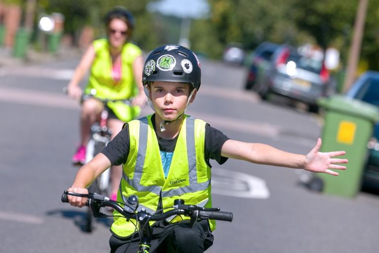 Young person cycling in the foreground with an adult cycling behind