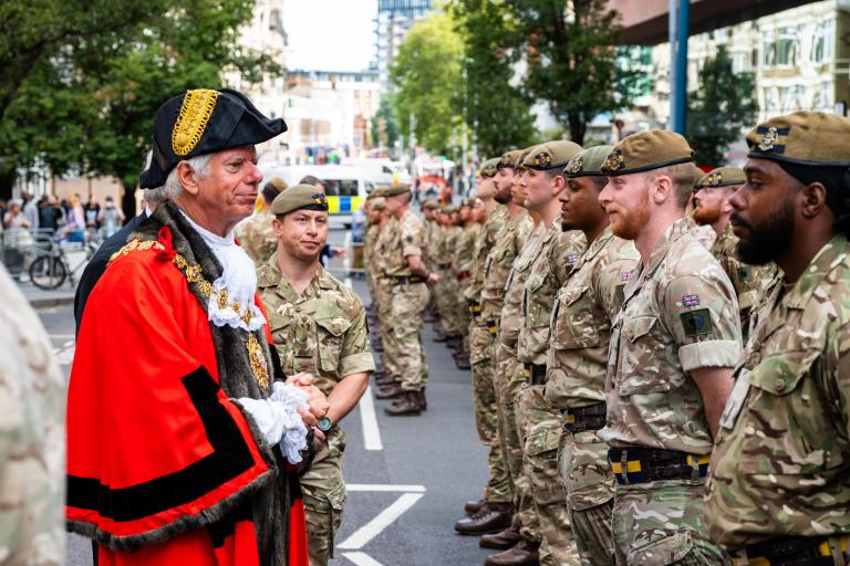Cllr David Gardner, the Mayor of the Royal Borough of Greenwich, in ceremonial dress meets to a line of uniformed soldiers in Wellington Street