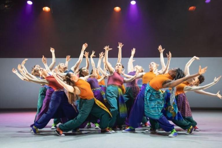 A group of dancers in a huddle with their arms up in the air