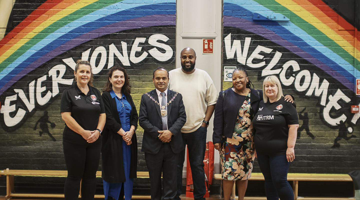 A group photo of youth hub staff and councillors standing in front of a painted mural wall which says 'everyones welcome'