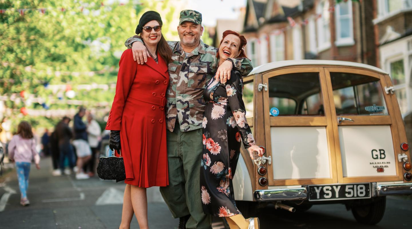 Three people in 40s clothing standing next to a vintage car