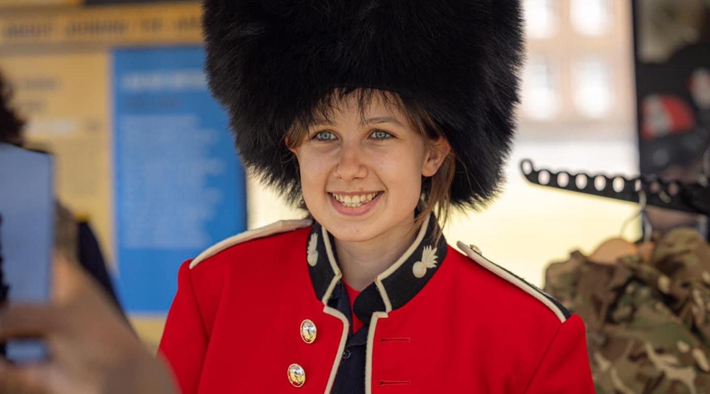 A person wearing a traditional red soldier jacket and black 'bearskin' hat