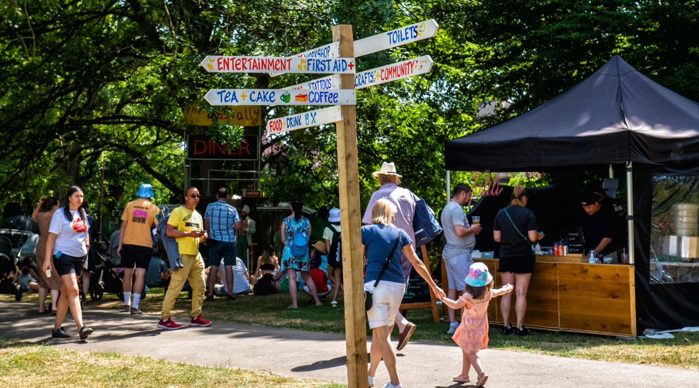 A sign post at an outdoor event, pointing in different directions as people walk past.