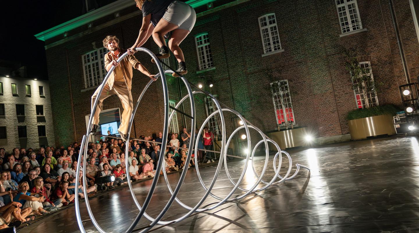 Performers on a metal frame in front of a crowd.