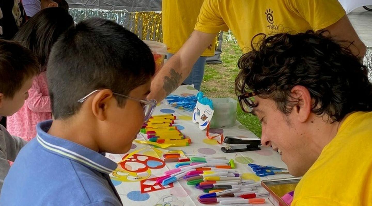 A group of adults in yellow tops helping young children to do arts and crafts at a table.